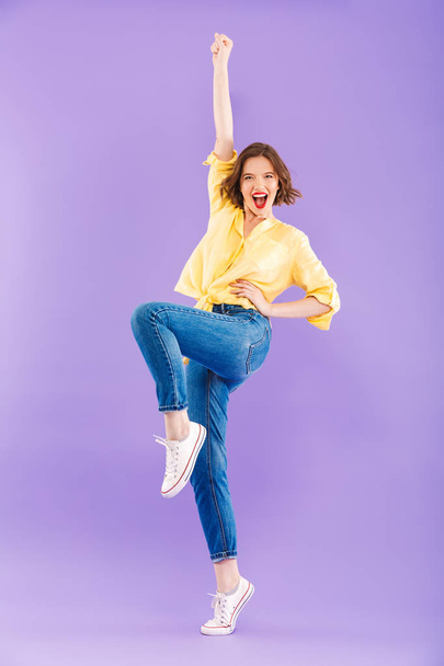 Full length portrait of a joyful young woman dressed in summer clothes celebrating success over violet background - Foto, afbeelding