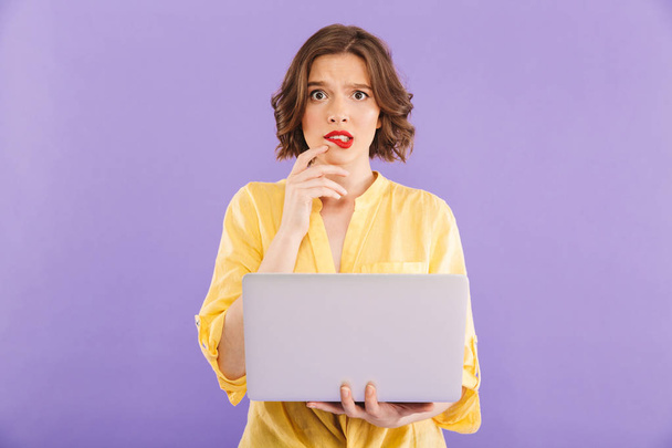 Image of confused woman isolated over purple wall background using laptop computer. - Photo, Image