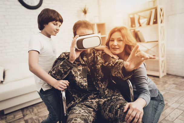 Paralyzed Male Soldier Family Are Having Fun. Meeting After War. Son And Wife. Camouflage Uniform. Virtual Reality Glasses. Paralyzed Soldier. Homecoming Concept. Return From Army. - 写真・画像