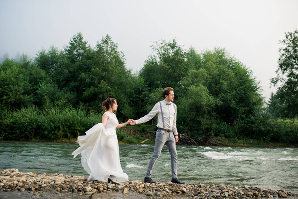 Beautiful bride and groom. Just merried. wedding couple. Happy bride and groom on their wedding walking and holding hands. bride and groom in mountains, beautiful nature, landscape, fog - Фото, изображение