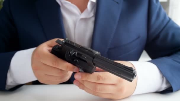 Closeup 4k záběry z podnikatel v obleku sedí za stolem v kanceláři a kontrola jeho zbraň. Muž spřádání revolver buben - Záběry, video