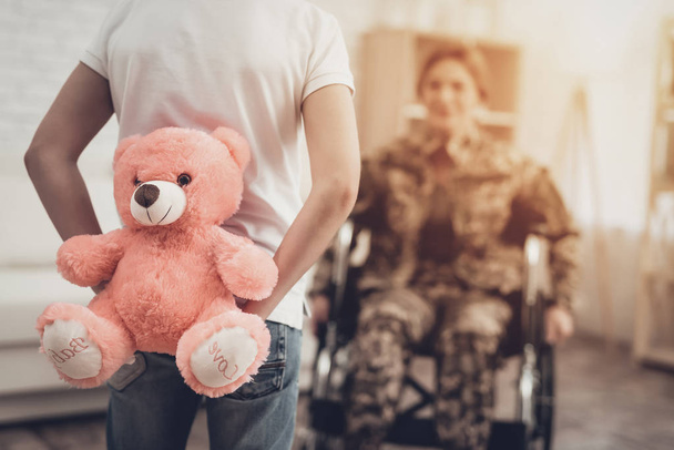 Woman Veteran In Wheelchair Homecoming Concept. Family Meeting. Leaving From War. Fluffy Toy. Camouflage Uniform. Son Hanging. Feelings Showing. Patriotic Comeback. Paralyzed Soldier. - Фото, изображение