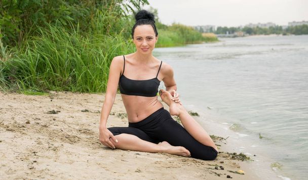 jonge vrouw doet yoga op de oever van de rivier - Foto, afbeelding