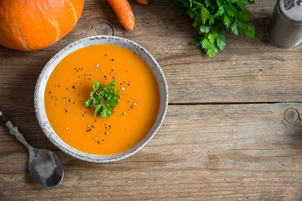 Pumpkin soup and organic pumpkins on wooden table. Seasonal autumn food - Spicy pumpkin and carrot soup in bowl. - Foto, Imagem