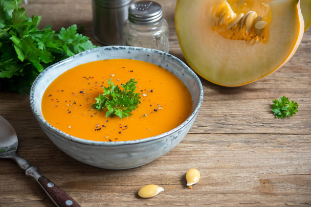 Tök leves és a fából készült asztal bio sütőtök. Szezonális őszi élelmiszer - fűszeres sütőtök leves tálban. - Fotó, kép