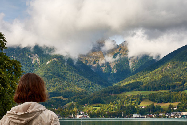 View of the lake near St. Wolfgang with a woman looking at the Alps mountains in the background, under a blue sky with clouds on a sunny day - Photo, Image