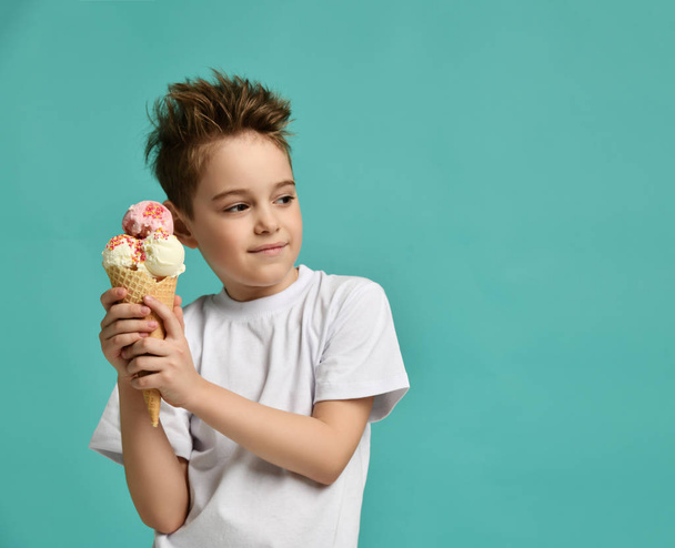 Baby boy kid hold strawberry vanilla ice cream in waffles cone happy smiling looking at the corner on blue mint background  - Foto, Imagem