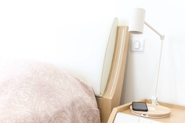 Wireless smartphone charging on lamp near bed - Zdjęcie, obraz