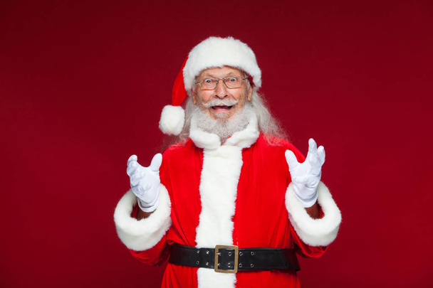 Christmas. Good Santa Claus in white gloves shows faces, grimaces, shows his tongue. Not standard behavior. Isolated on red background. - Valokuva, kuva