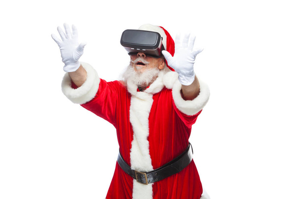 Christmas. Santa Claus in black virtual reality glasses makes gestures with his hands. Surprise, emotion. New technology. Isolated on white background. - Foto, Bild