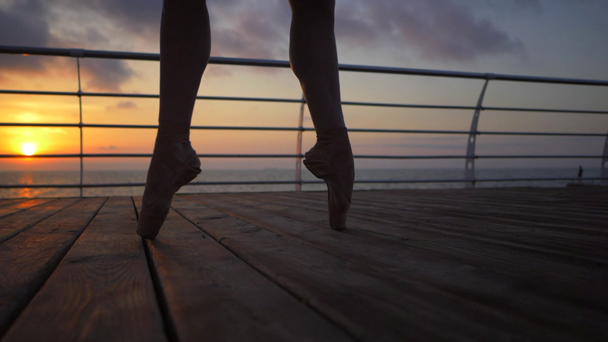 Detailní záběr nohou tanečníků baletu jak ona trénuje pointe cvičení na dřevěné nábřeží nedaleko moře, silueta Zenske nohy v pointe boty. Baletka ukazuje klasický balet pas. Zpomalený pohyb. - Záběry, video