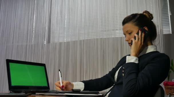 Empresária uma mesa de escritório na frente de um laptop com uma tela verde falando no telefone
 - Filmagem, Vídeo