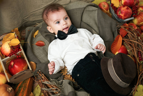 концепція осені - хлопчик лежить на жовтому листі з фруктами та вегетаріанцями, червоними яблуками та гарбузами
 - Фото, зображення
