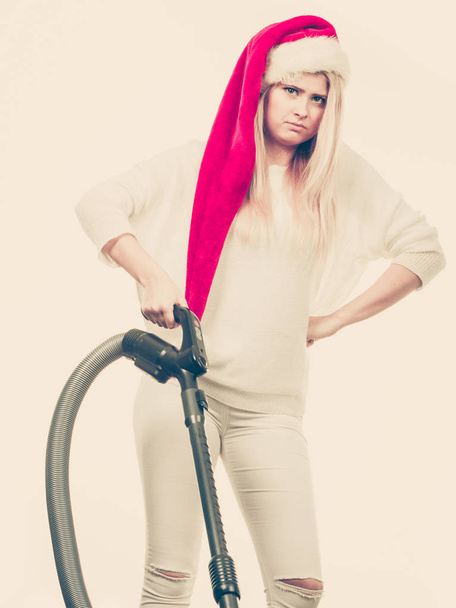 Woman vacuuming the house. Funny angry teen girl in santa helper hat with vacuum cleaner. Christmas time and housework concept. - Foto, Imagen