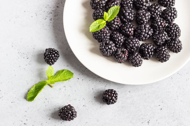 Fresh blackberries on a plate with mint leaves on light gray stone background. Top view, copy space. - Fotoğraf, Görsel