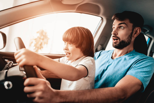 Man With Kid Are Sitting At The Wheel Of New Vehicle. Smiling Family. Car Buying In A Showroom. Automobile Salon. Cheerful Driver. Happy Together. Father And Son. Good Mood. Great Trade. - Fotografie, Obrázek