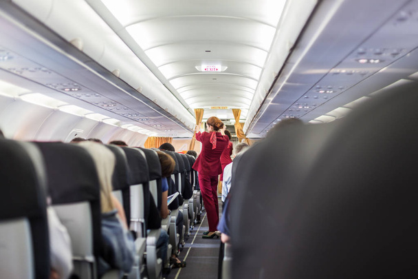 Αεροσυνοδός με κόκκινο στολή δίνοντας οδηγίες ασφαλείας για τους εμπορικούς επιβάτες αεροπλάνο. - Φωτογραφία, εικόνα
