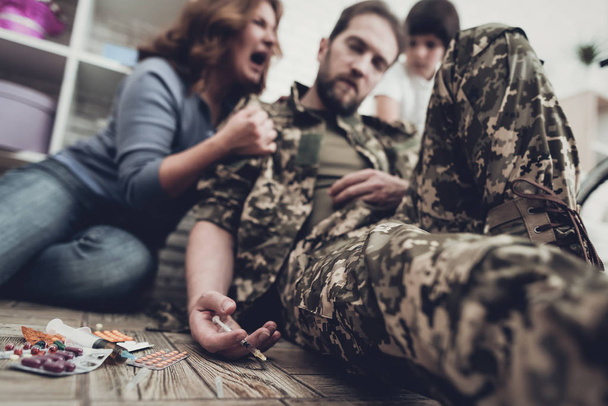 Disable Veteran Lays On Floor. Narcotic Overdose. Syringe In Hand. Pills On The Floor. Frightened Family. Camouflage Uniform. Disappointed Hero. Paralyzed Soldier. Depression Problem. - Photo, Image