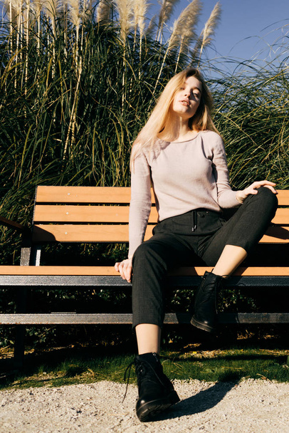 fiduciosa giovane ragazza in posa su una panchina di legno al sole, street style e moda
 - Foto, immagini