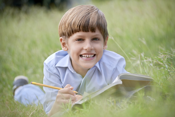 chłopiec szczęśliwy szkoła odrabiania lekcji i uśmiechnięty, leżąc na trawie - Zdjęcie, obraz