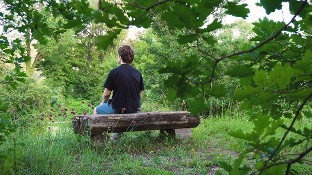 Mladý muž sedí na staré dřevěné lavičce v parku - Fotografie, Obrázek