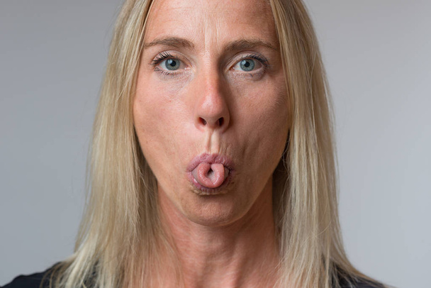 Zralá žena trčí její jazyk na kameru v gesto neslušné pohrdavý zblízka oříznutý obličej portrét - Fotografie, Obrázek