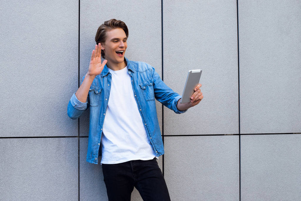 ¡Hola amigo! Vista lateral del joven guapo usando su touchpad con sonrisa mientras está parado al aire libre
 - Foto, imagen
