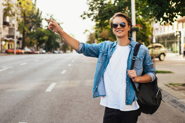 Taxi! Handsome young man getting a taxi with smile while walking outdoors with smile  - 写真・画像