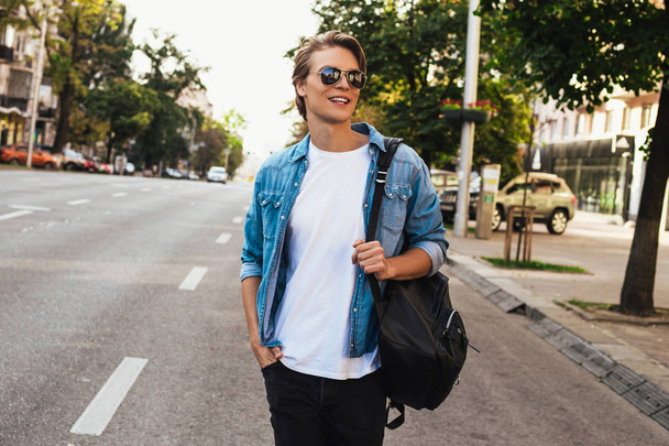 Το στυλ του δρόμου. Όμορφος νεαρός άνδρας ψάχνει μακριά ενώ το περπάτημα σε εξωτερικούς χώρους με χαμόγελο  - Φωτογραφία, εικόνα