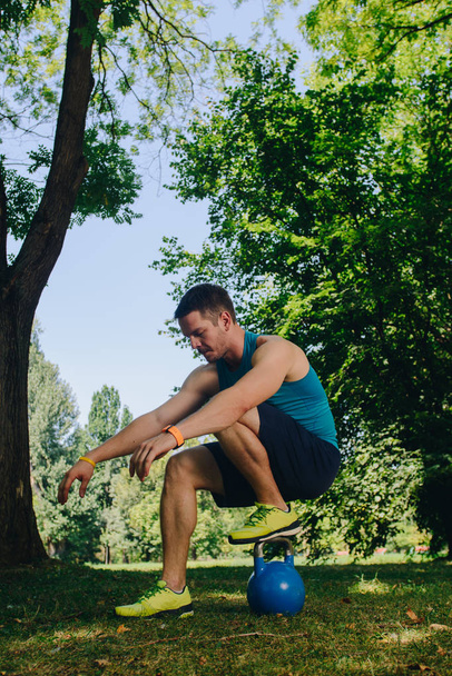 Sportlicher Mann streckt seine Beine auf der Kettlebell in der Natur aus - Foto, Bild
