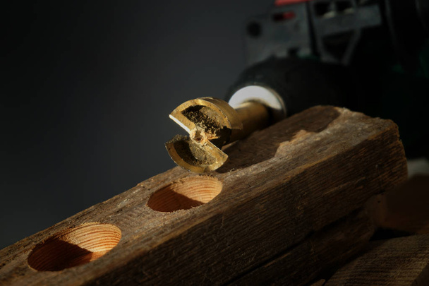 Fechar em pequena ferramenta de metal para a perfuração de furos circulares sentados em cima do bloco de madeira sobre fundo preto
 - Foto, Imagem