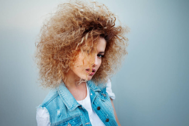 Jonge aantrekkelijke vrouw met zeer weelderige haren. Portret van een mooi meisje in denim vest - Foto, afbeelding