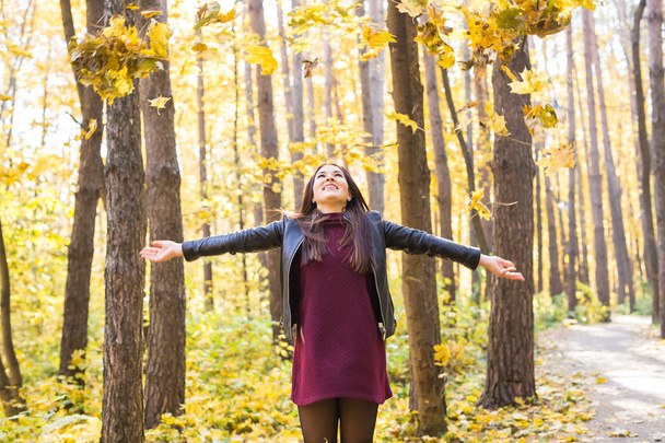 秋、喜びと人コンセプト - 秋の公園で楽しんで若い女性。彼女は空に黄色の葉を投げています。 - 写真・画像