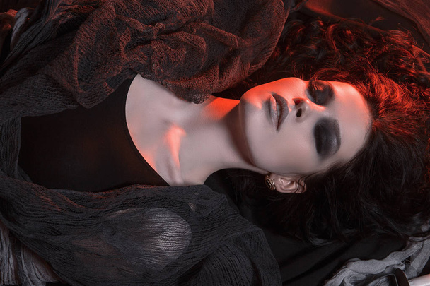beautiful young woman with make-up on the floor.halloween style smokey eyes beauty girl wrapped in rags. mummy in red color light - Foto, immagini
