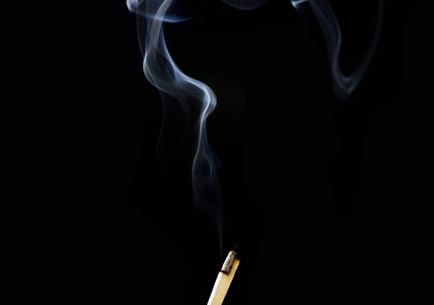 O bastão de incenso está queimando no fundo preto. Fumaça de pau de incenso
 - Foto, Imagem