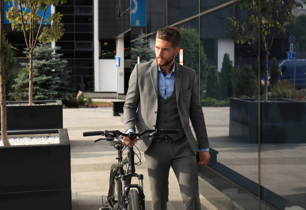 Confident young businessman walking with bicycle on the street in town. - Photo, image