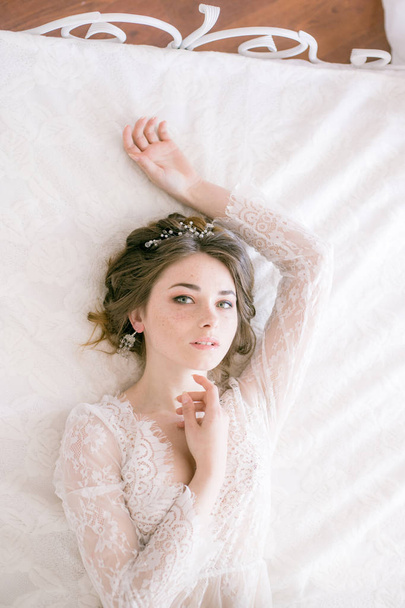 Portrait of beautiful bride. Morning of the bride. Wedding morning. Makeup. Bride with cones and fair hair. Fragile bride in white lace negligee - Foto, afbeelding