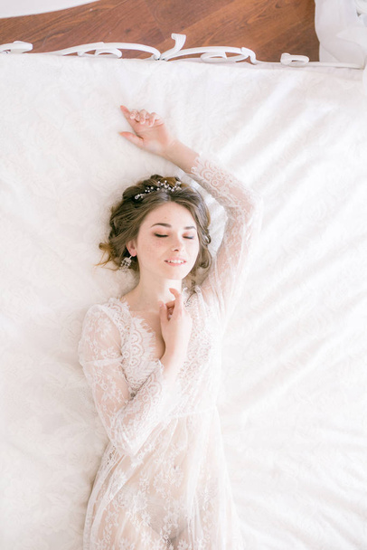 Portrait of beautiful bride. Morning of the bride. Wedding morning. Makeup. Bride with cones and fair hair. Fragile bride in white lace negligee - Fotoğraf, Görsel