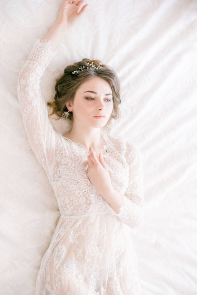 Portrait of beautiful bride. Morning of the bride. Wedding morning. Makeup. Bride with cones and fair hair. Fragile bride in white lace negligee - Fotó, kép