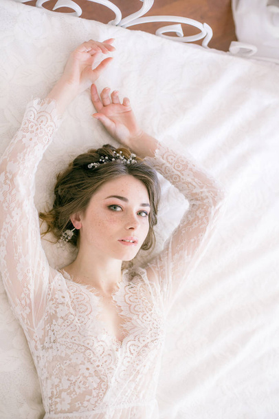 Portrait of beautiful bride. Morning of the bride. Wedding morning. Makeup. Bride with cones and fair hair. Fragile bride in white lace negligee - Foto, imagen