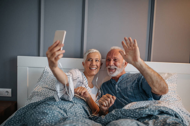 Elderly couple lying in bed holding a mobile phone - Zdjęcie, obraz