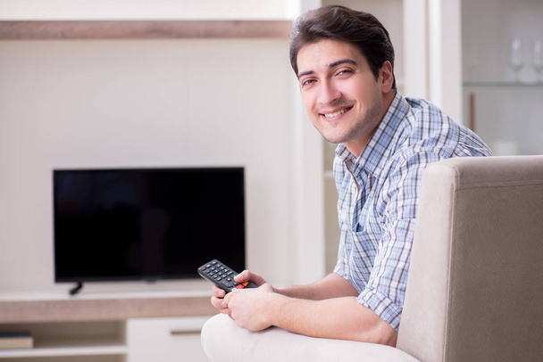 Молодой человек смотрит телевизор дома - Фото, изображение