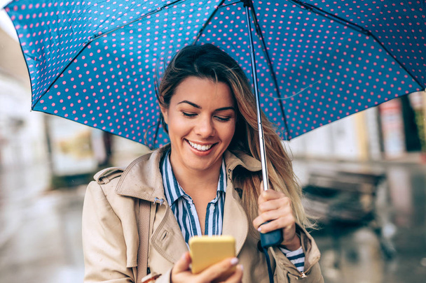 雨の日に彼女の携帯電話を使用して若い女性 - 写真・画像