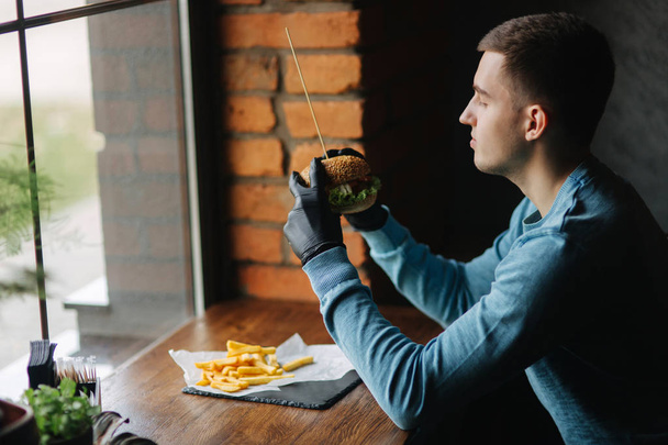 Человек в черных перчатках берет бургер в руки
 - Фото, изображение