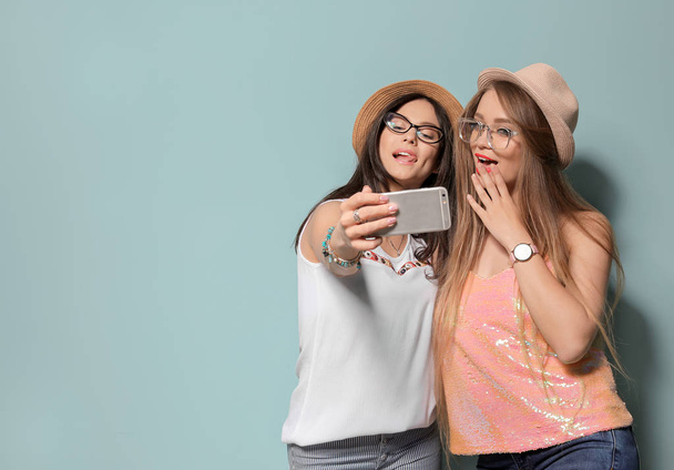 Atractivas mujeres jóvenes tomando selfie sobre fondo de color
 - Foto, Imagen
