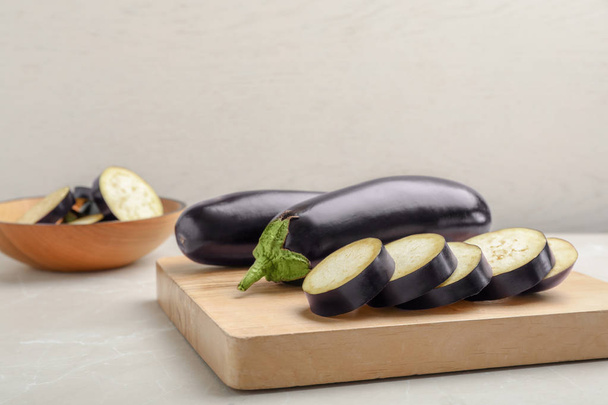 Wooden board with ripe eggplants on table - Foto, afbeelding