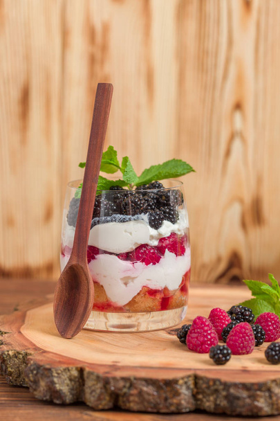 Trifle close up photography with fresh multi layered dessert with dairy and ripe raspberries and blackberries on wooden background - sweet organic healthy food with fruits. - Foto, afbeelding