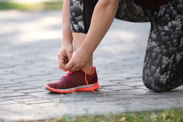 Young woman tying shoelaces before running in park, focus on legs - Foto, afbeelding