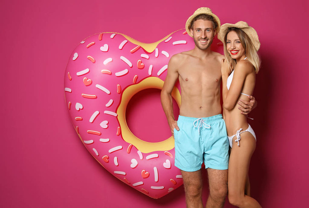 Happy young couple in beachwear with inflatable ring and cocktail on color background - Foto, afbeelding