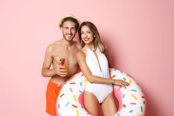 Happy young couple in beachwear with inflatable ring and cocktail on color background - Foto, imagen